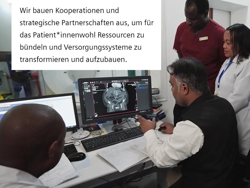 Ärzte beraten sich im Scanning Kontrollraum vor einem Computer Bildschirm, auf dem Scanning Aufnahmen zu sehen sind.