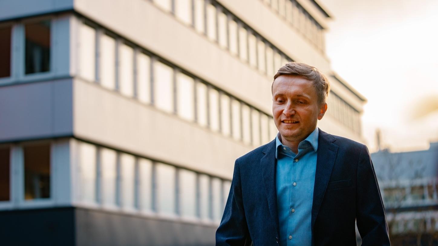 Adam Strzelecki walking in front of the office in Baden. The sun sets behind him.