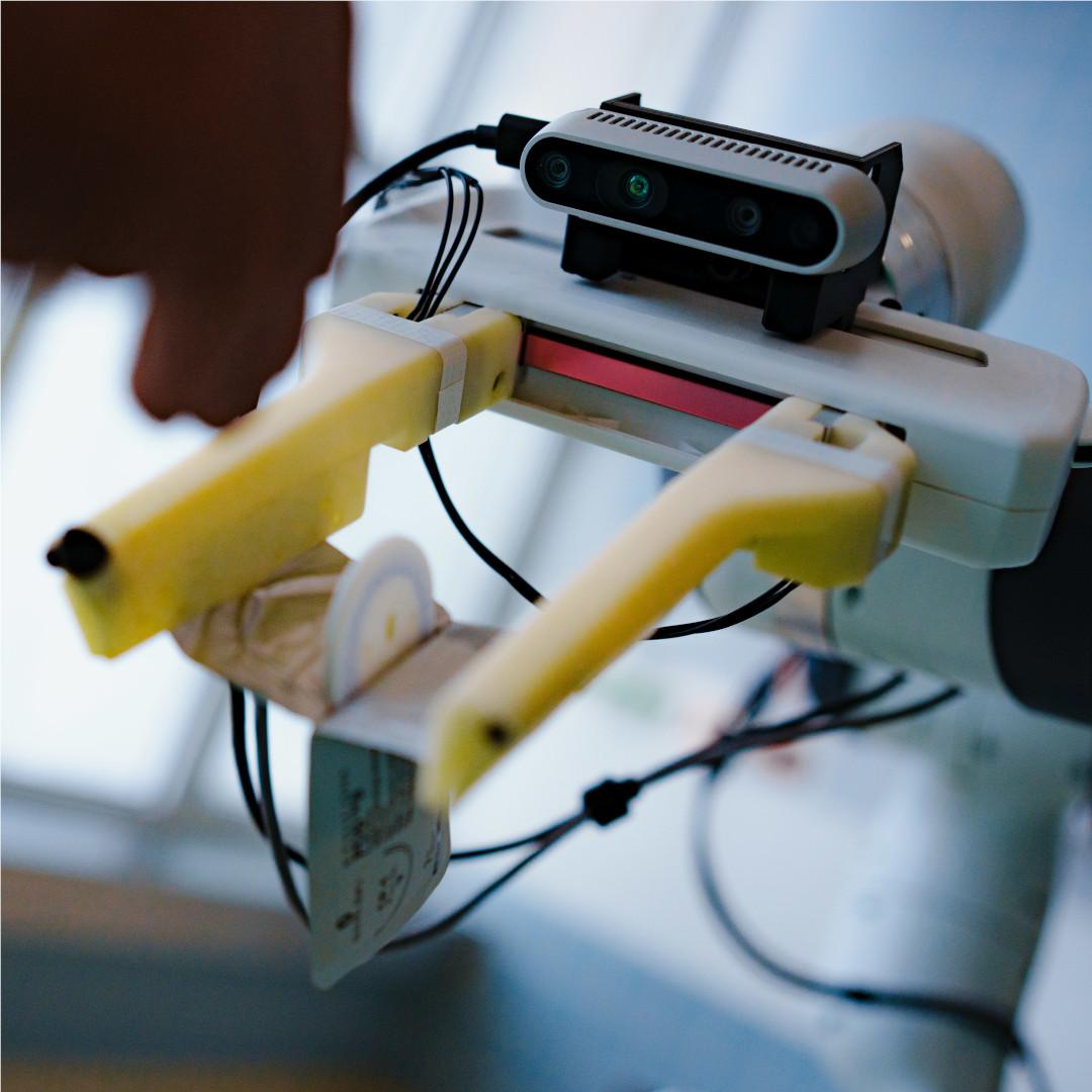 Nahaufnahme der RGBD-Kamera und des Greifers des Prototyps des AURORA-Assistenzroboters. Der Roboter öffnet die sterile Verpackung eines chirurgischen Nahtsets.