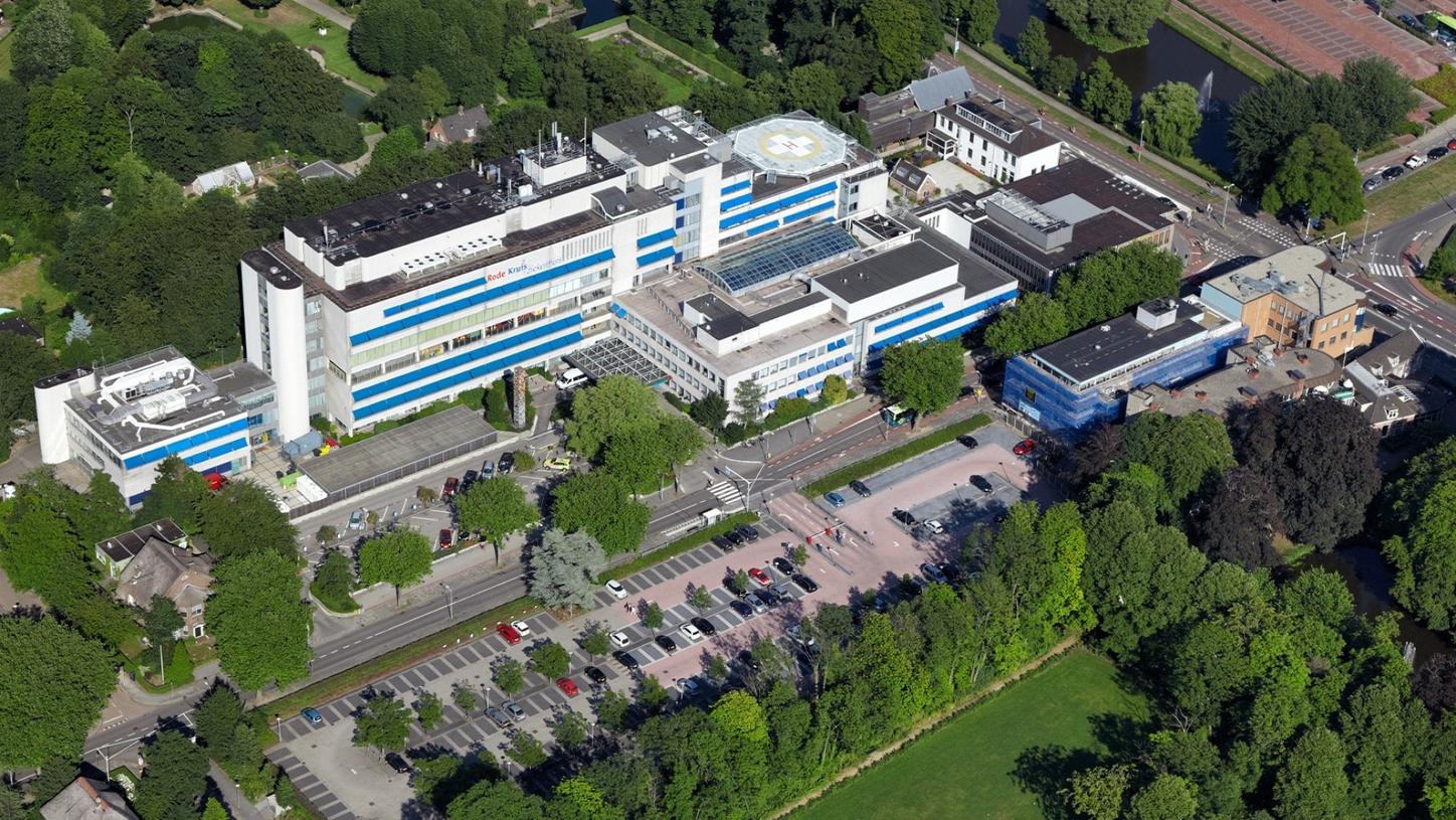 We see an aerial view of the "Rode Kruis" hospital in Beverwijk, the Netherlands. The building is surrounded by trees and meadows. 