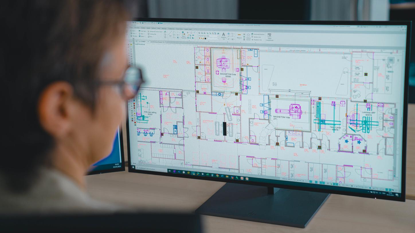 Stefanie Vonhoff sits in front of her computer screen. She is only vaguely recognizable from behind in the foreground. The focus is on the screen with the CAD software on it, which shows an architectural floor plan.