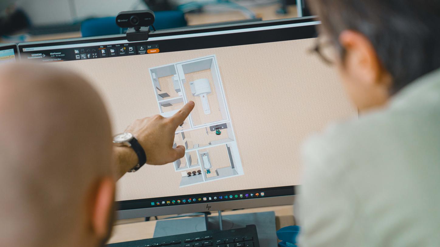 The photo shows a close-up of architect Stefanie Vonhoff and IT and 3D expert Matthias Brenner. Both are leaning over the screen of a computer. A 3D model of an architectural floor plan can be seen on the screen. Matthias Brenner points to the plan.