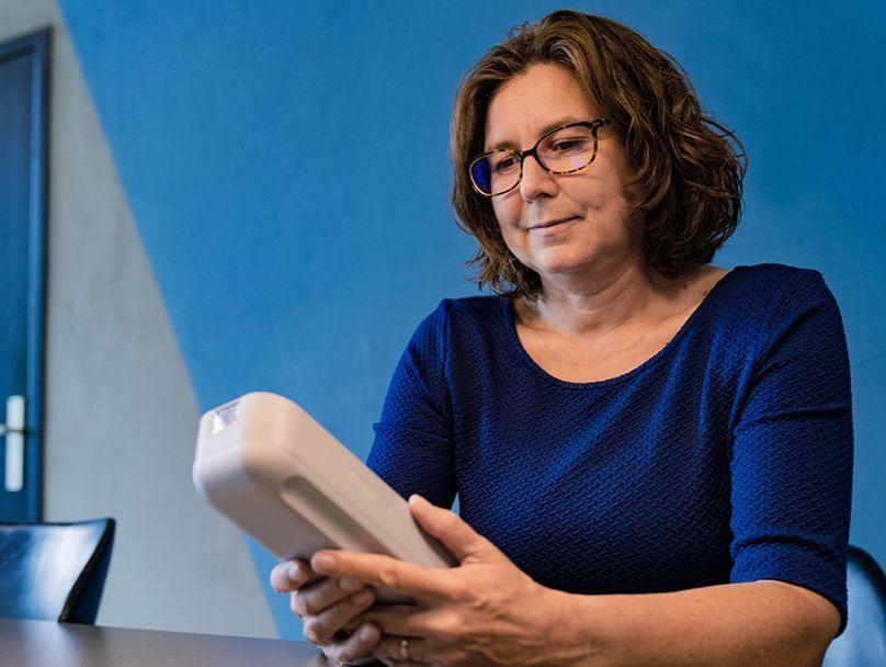 Femke sitting at a table, holding in her hands the handheld device for troponin testing that she developed together with her team
